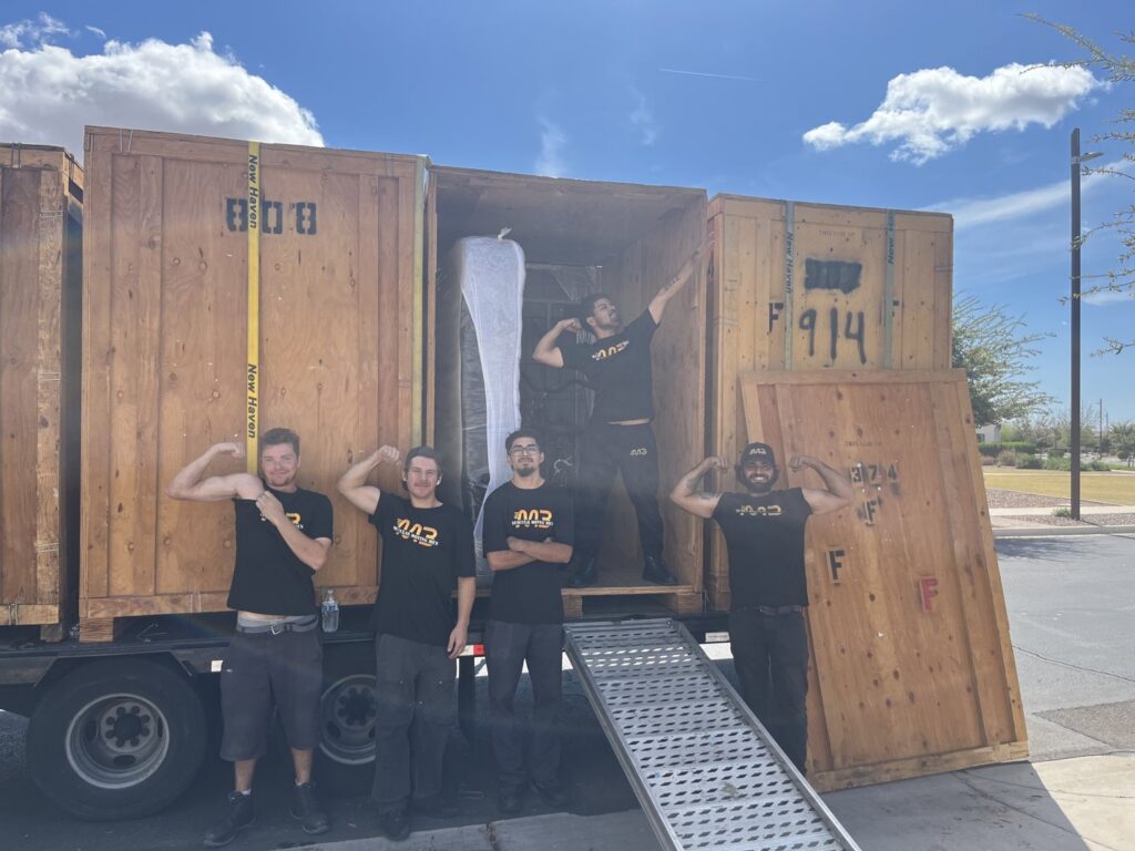Five Muscular Moving Men & Storage movers posing with a truck loaded with wooden crates and a ramp in Phoenix, AZ.