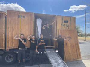 Five Muscular Moving Men & Storage movers posing with a truck loaded with wooden crates and a ramp in Phoenix, AZ.