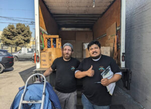 Two movers from Cheap Movers Los Angeles standing at the back of a moving truck filled with boxes and equipment in Los Angeles, CA.