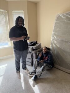 Two TruMoving movers in a room with a plastic-wrapped mattress, ready for transport in Lakewood, CO.