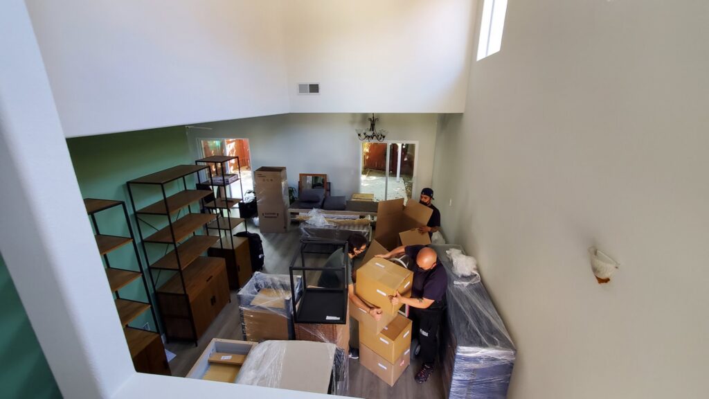 Movers from Cheap Movers Los Angeles actively moving boxes and furniture in a large, high-ceilinged room in Los Angeles, CA.