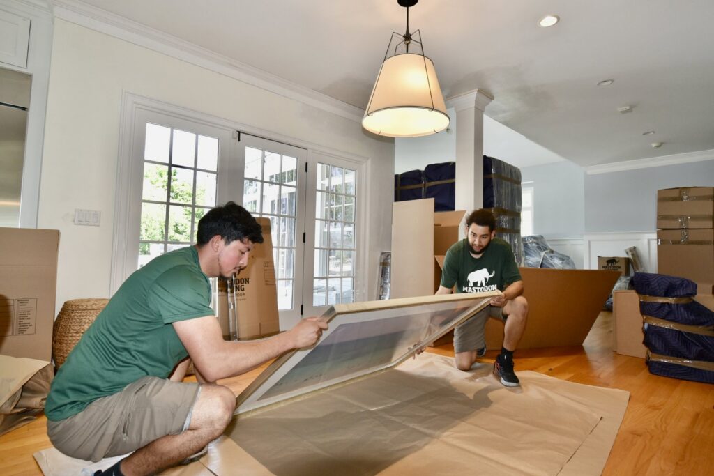 Two Mastodon Moving LLC movers carefully wrapping a large framed item on the floor in Westborough, MA.