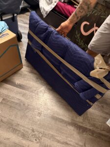 Professional movers carefully wrapping a piece of furniture with a blue moving blanket and tape, provided by Houston Affordable Movers in Houston, TX.