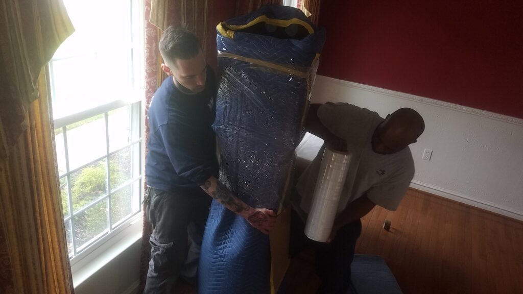Two movers carefully wrapping and moving a large item, showcasing professional service from S&P Network's Marathon Moving Solutions in Mechanicsburg, PA.