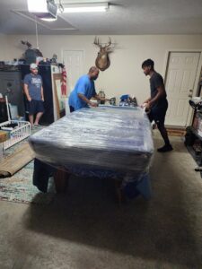 Ron's Moving team carefully wrapping a pool table in a garage for transport in Little Rock, AR.