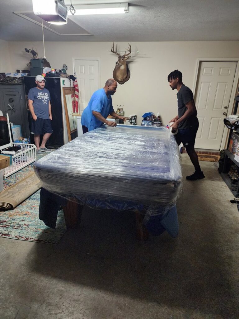 Ron's Moving team carefully wrapping a pool table in a garage for transport in Little Rock, AR.