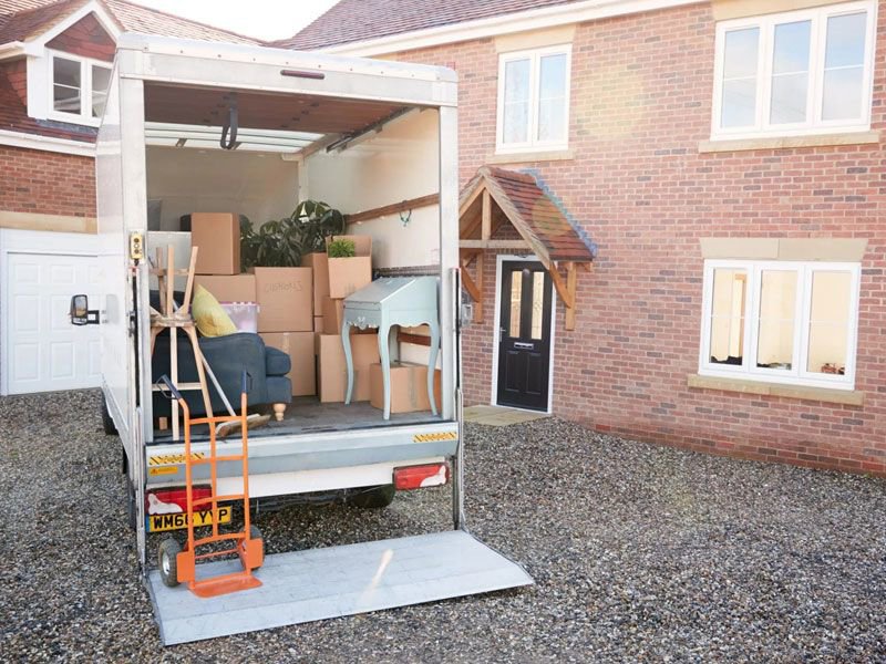 The back of a moving truck being loaded with furniture and boxes outside a brick house by Las Vegas Moving Pros LLC in Las Vegas, NV.