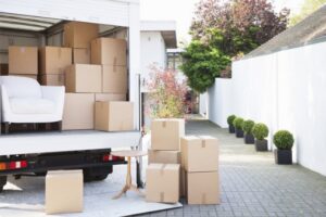 A moving truck being unloaded with boxes and furniture outside a modern house by Las Vegas Moving Pros LLC in Las Vegas, NV.