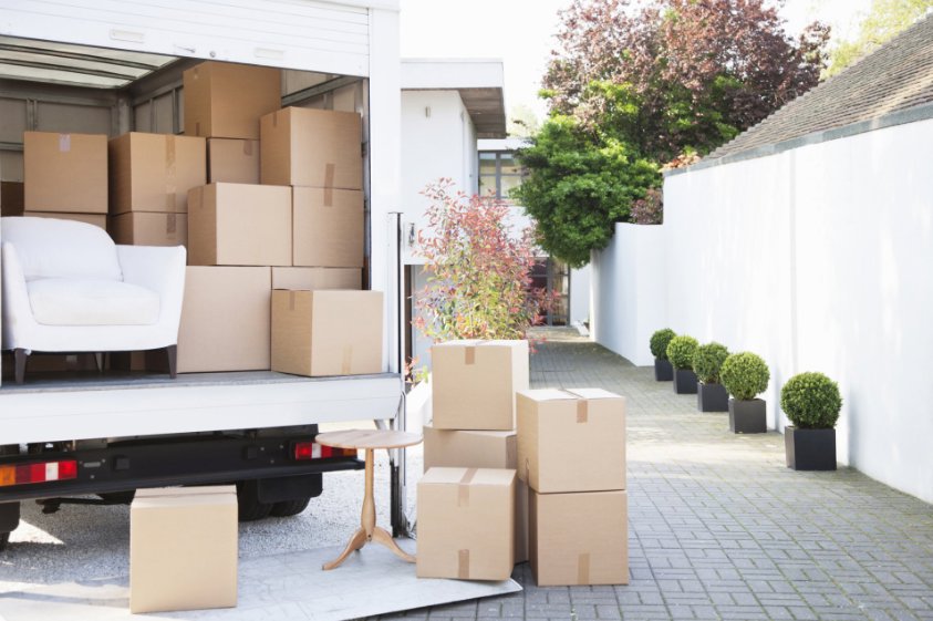 A moving truck being unloaded with boxes and furniture outside a modern house by Las Vegas Moving Pros LLC in Las Vegas, NV.