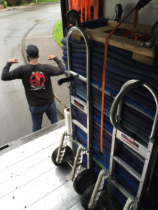 An open moving truck loaded with moving blankets and hand trucks, with a mover flexing outside for Able Movers in Hillsboro, OR.