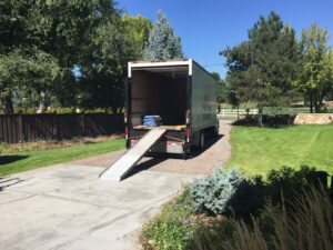 A TruMoving truck with its ramp extended and moving blankets inside, parked in a residential driveway in Lakewood, CO.