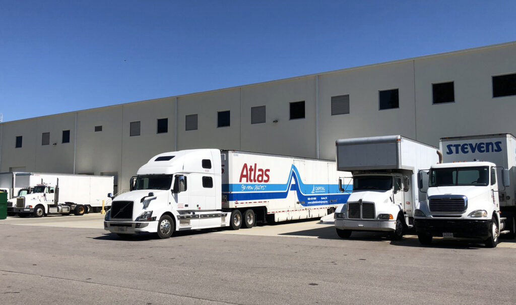 Multiple moving trucks, including Capital Relocation Group and Atlas, parked at a commercial facility in Raleigh, NC.