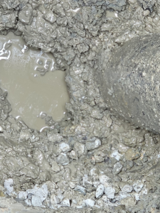 A close-up view of muddy, wet ground and a pipe, indicating a water damage issue addressed by Western Iowa Utilities in Council Bluffs, IA.