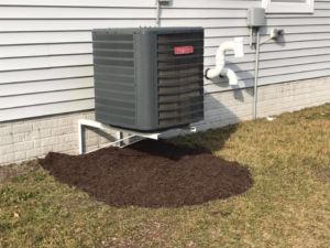 Dark brown mulch neatly placed around an outdoor air conditioning unit next to a house, a service by Mike's Lawn Care Service in Dover, DE.