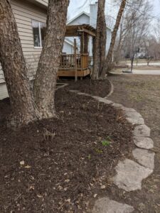 Freshly mulched tree beds with a decorative stone border, showcasing detailed yard maintenance by Nice & Precise Lawn Care in Ames, IA.
