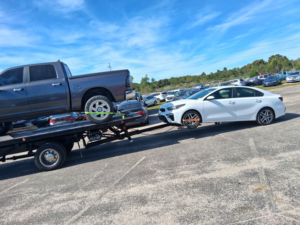 A flatbed tow truck from AMC Towing in Mobile, AL, transporting a pickup truck and towing a sedan behind it.