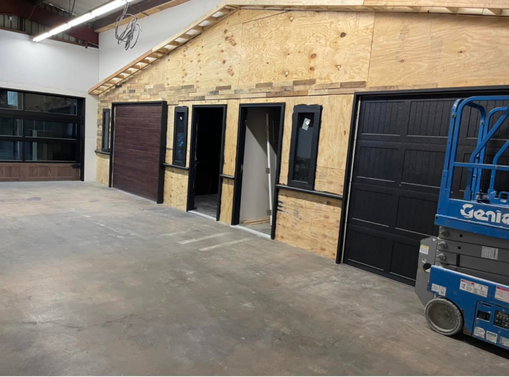 Multiple garage doors, including black and wood-grain styles, installed in a showroom or training area at AMR Distribution Center in Wichita, KS