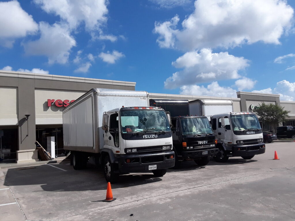 Multiple moving trucks parked outside a commercial building, ready for service by Emanuel Movers, Inc. in Houston, TX