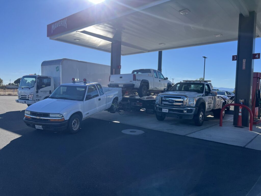 Multiple tow trucks from Kennedy Towing & Transport in Anderson, CA, transporting pickup trucks at a gas station.