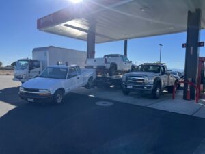 Multiple tow trucks from Kennedy Towing & Transport in Anderson, CA, transporting pickup trucks at a gas station.