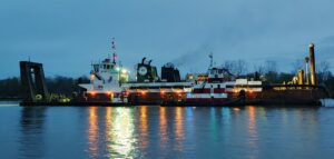 Multiple tugboats from Myrick Marine Contracting Corp. in Norfolk, VA, towing a large crane barge at dusk.