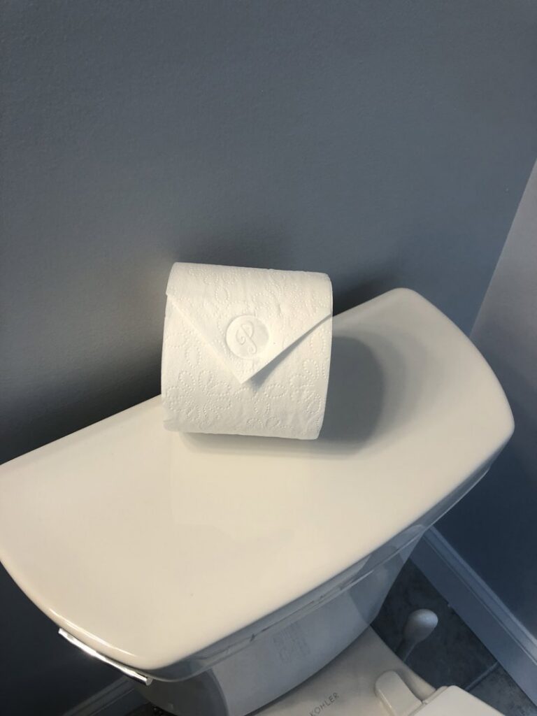 A neatly folded toilet paper roll with a decorative 'P' stamp, a signature touch from Polished Housekeeping Services in Londonderry, NH.