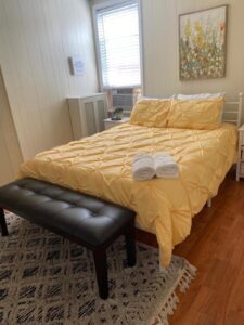 A neatly made bed with a yellow comforter and folded towels in a clean bedroom, demonstrating house cleaning services by Rivas Molina's Cleaning LLC in Dundalk, MD.