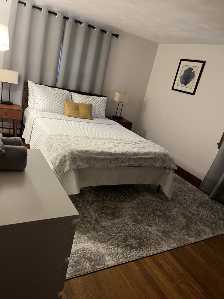 A neatly made bedroom with crisp white bedding and a patterned rug, showcasing a clean space by Make It Shine in Worcester, MA