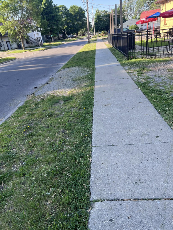 A neatly mowed grass strip along a sidewalk, showing completed work by Vick's Lawn Care Service in Des Moines, IA.