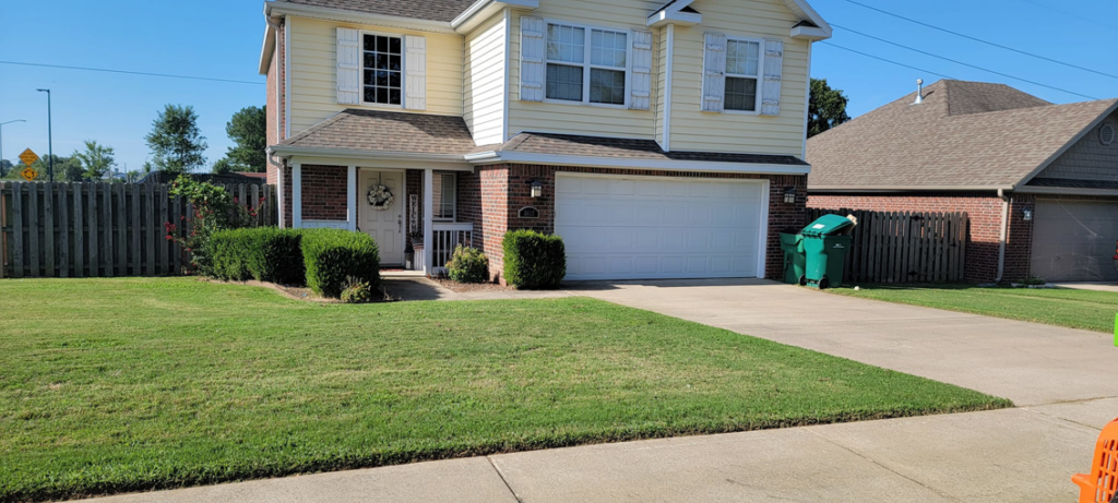 A neatly mowed lawn and trimmed bushes in front of a residential home by Reap What You Mow Lawn Care LLC in Springdale, AR.