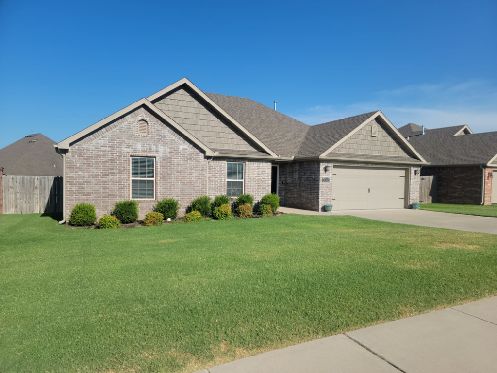 A neatly mowed and edged lawn in front of a brick house by Reap What You Mow Lawn Care LLC in Springdale, AR