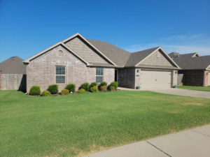 A neatly mowed and edged lawn in front of a brick house by Reap What You Mow Lawn Care LLC in Springdale, AR