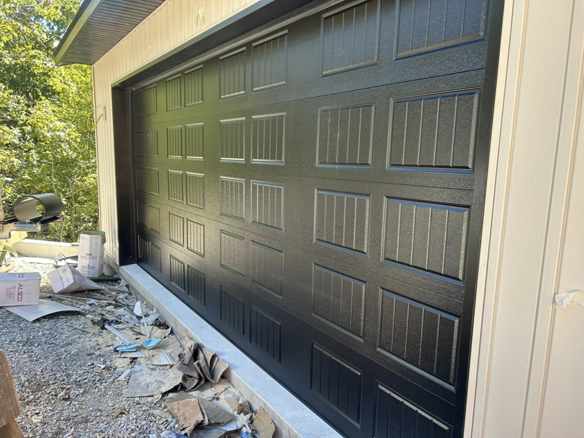 A newly installed black panel garage door on a building exterior by Complete Garage Solutions NWA in Centerton, AR.
