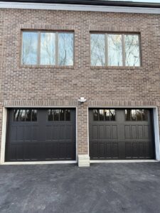 Two newly installed black garage doors on a brick house by Mascolo Overhead Doors & Maintenance in Brookfield, CT.