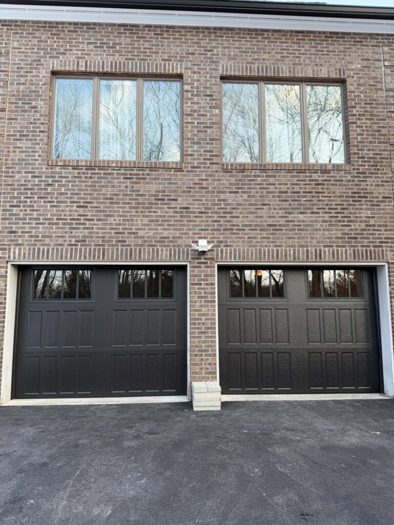 Two newly installed black garage doors on a brick house by Mascolo Overhead Doors & Maintenance in Brookfield, CT.