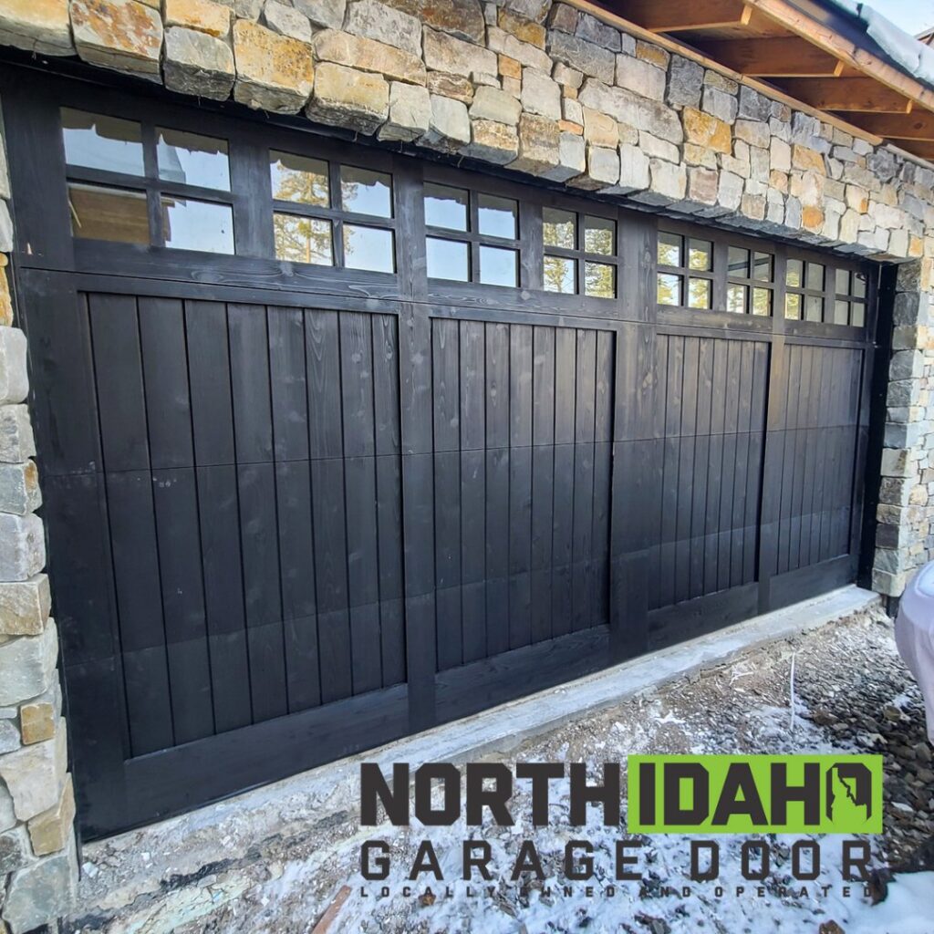 A newly installed black garage door with multiple window panels on a stone-faced building by North Idaho Garage Door in Coeur d'Alene, ID.