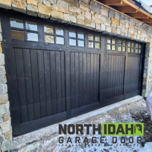A newly installed black garage door with multiple window panels on a stone-faced building by North Idaho Garage Door in Coeur d'Alene, ID.