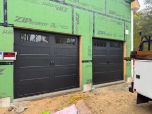 Two new black garage doors with windows installed on a construction site by J.A. Overhead Door in Westfield, MA.