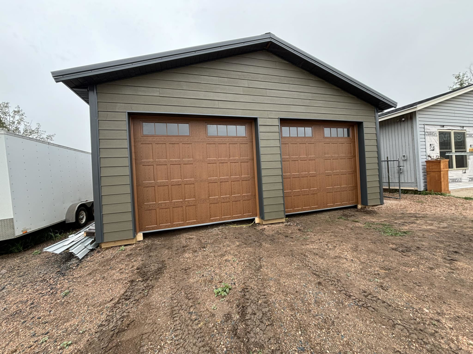 Two newly installed brown garage doors with windows on a modern detached garage by Laramie Garage Doors in Laramie, WY.