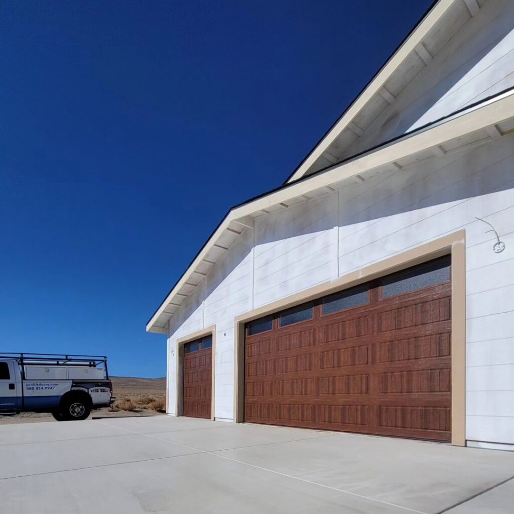 Two new brown garage doors installed on a white house by 775 Overhead Doors in Carson City, NV, with a work truck nearby.