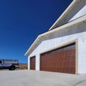 Two new brown garage doors installed on a white house by 775 Overhead Doors in Carson City, NV, with a work truck nearby.