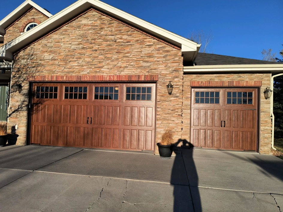 Newly installed brown garage doors with decorative windows on a stone house by Doors & more,inc in Quincy, IL