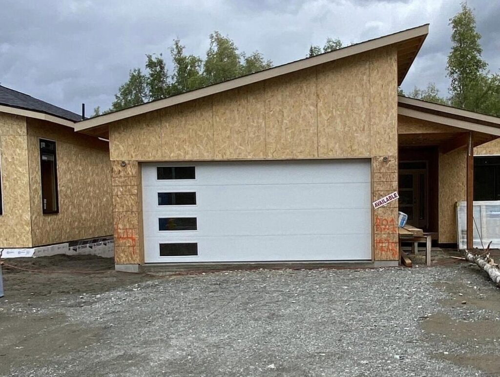 A newly installed white garage door with windows on a house under construction by Elite Doors in Wasilla, AK.