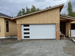 A newly installed white garage door with windows on a house under construction by Elite Doors in Wasilla, AK.