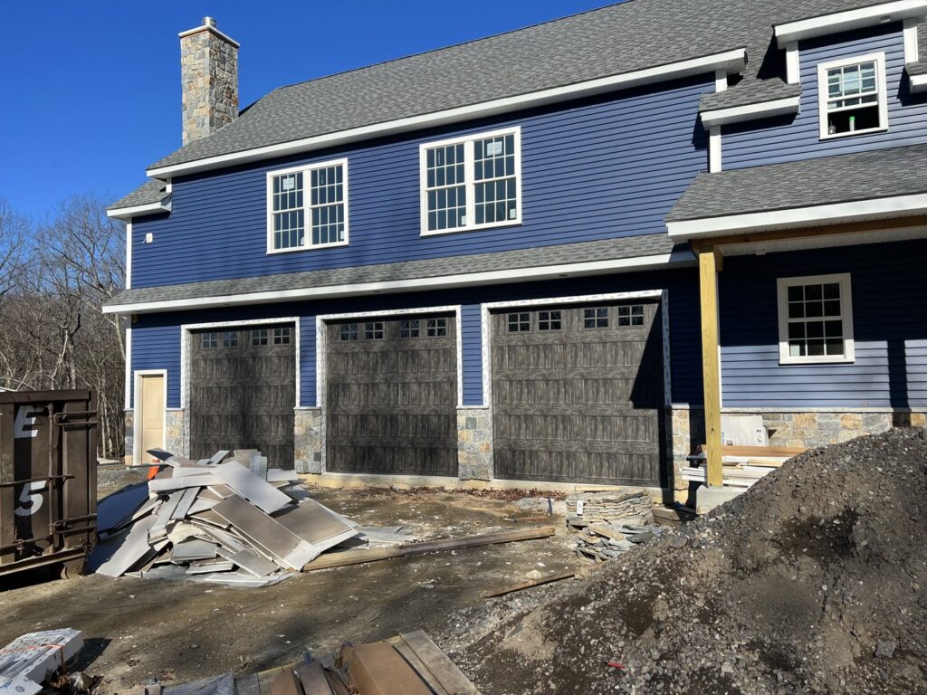Three dark brown garage doors installed on a new construction blue house by RidgeLine Overhead Garage Door of CT in Danbury, CT