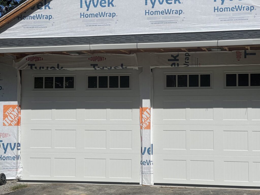 Two white garage doors installed on a house under construction, showcasing work by RidgeLine Overhead Garage Door of CT in Danbury, CT