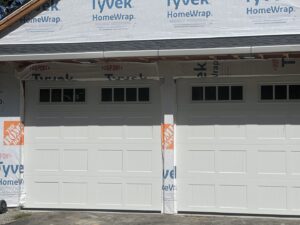 Two white garage doors installed on a house under construction, showcasing work by RidgeLine Overhead Garage Door of CT in Danbury, CT
