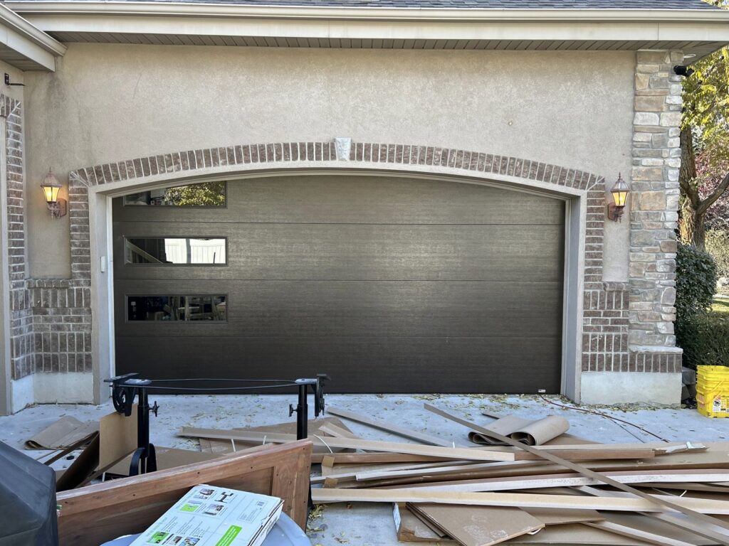 A newly installed dark brown garage door with horizontal windows, part of a construction project by Delta Garage Door in Millcreek, UT.