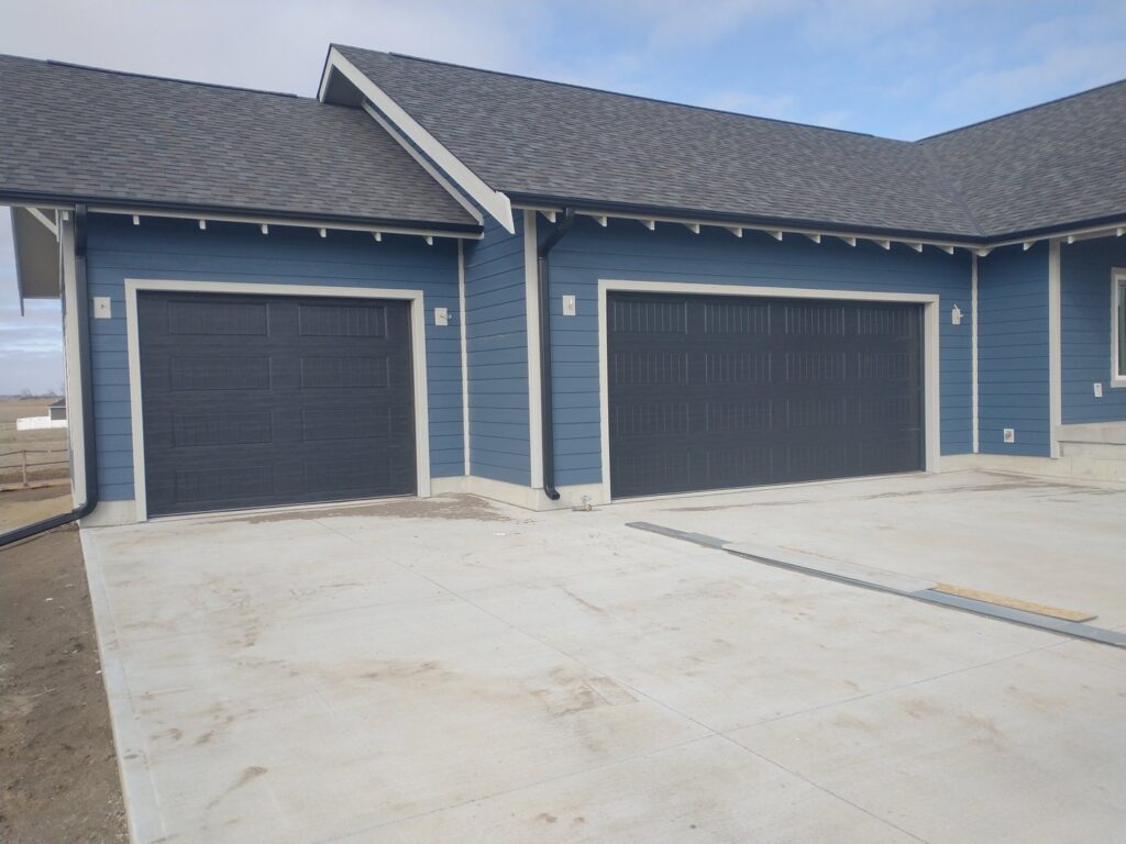 Two newly installed dark gray garage doors on a modern blue house by Bob McDonald Garage Door LLC in Columbus, NE.
