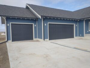Two newly installed dark gray garage doors on a modern blue house by Bob McDonald Garage Door LLC in Columbus, NE.